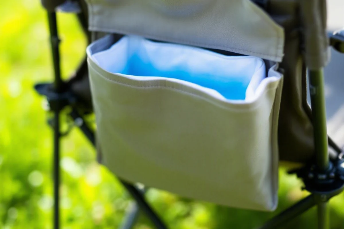 A folding camp chair with a cooler pocket on a grassy lawn.